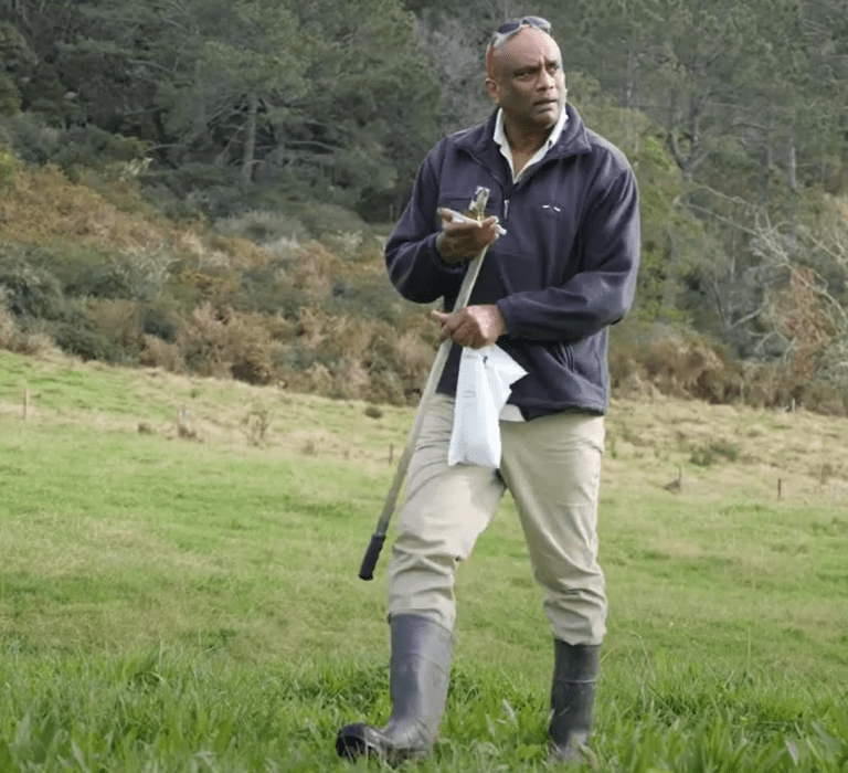 Dr. Gordon Rajendram conducting soil testing in a New Zealand pasture with field equipment.