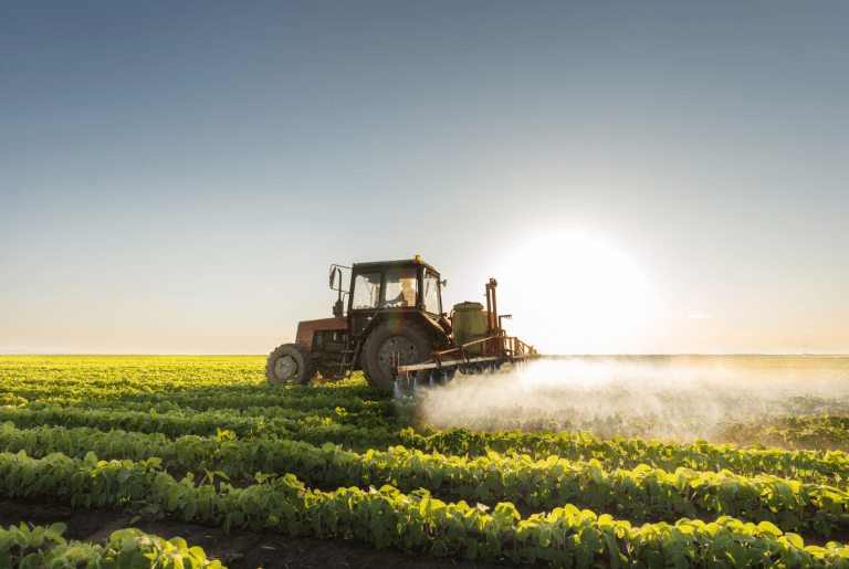 Tractor spraying fertilizer on crops in a New Zealand farm at sunrise